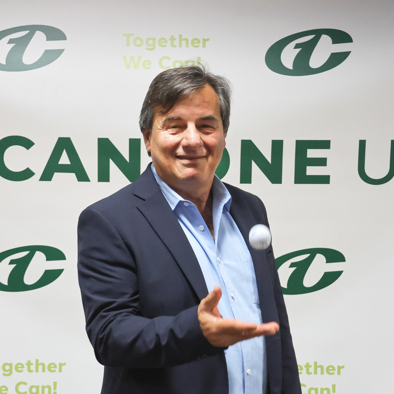 Male Can-One employee standing in front of Can-One logo wall